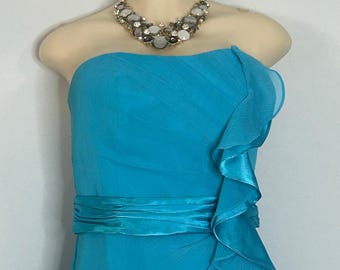 May include: A strapless turquoise dress with a ruffled side detail and a matching satin sash. A sparkling statement necklace with gray and clear stones is displayed on a mannequin.
