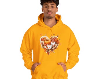 Könnte beinhalten: Ein gelber Hoodie mit einem herzförmigen Design, das einen Gnome, einen Kürbis, Pilze und eine Tasse Kaffee zeigt. Das Design ist von Herbstblättern umgeben.