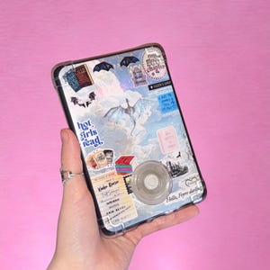 Peut inclure: Coque de téléphone transparente décorée d'autocollants représentant un dragon, des livres et le texte "hot girls read". Comprend un support de téléphone. Le tout sur fond rose.