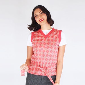 May include: A pink and white argyle patterned sweater vest with a V-neck and a matching pink belt tied at the waist.
