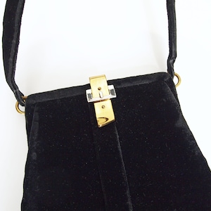 Puede incluir: Un bolso de noche de terciopelo negro con un cierre dorado y plateado.
