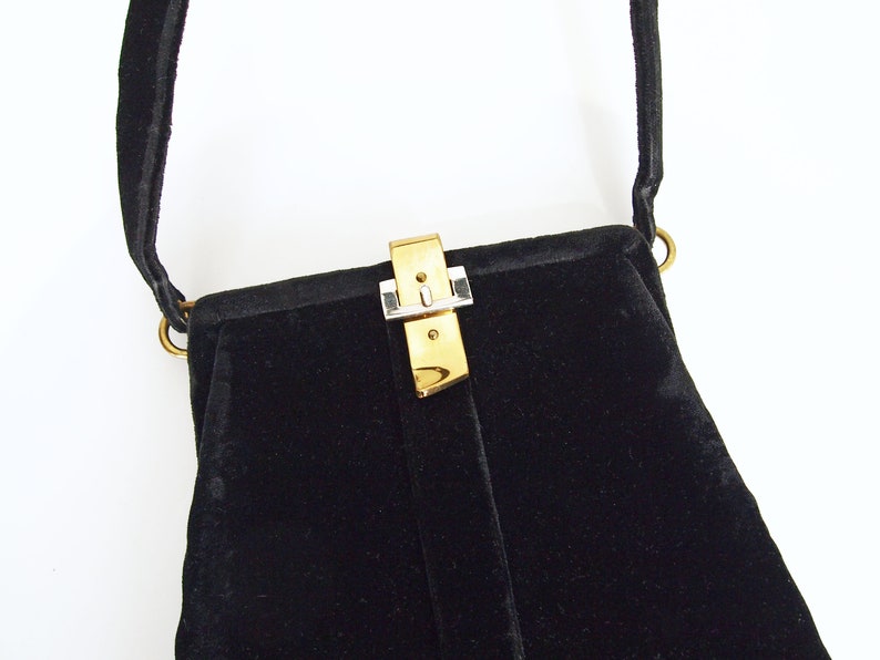 Puede incluir: Un bolso de noche de terciopelo negro con un cierre dorado y plateado.