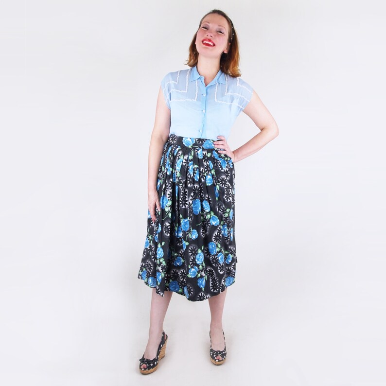May include: A light blue short-sleeved blouse with white trim and a black and blue floral print skirt. The skirt features a repeating pattern of blue roses and white accents. The outfit is a vintage style.