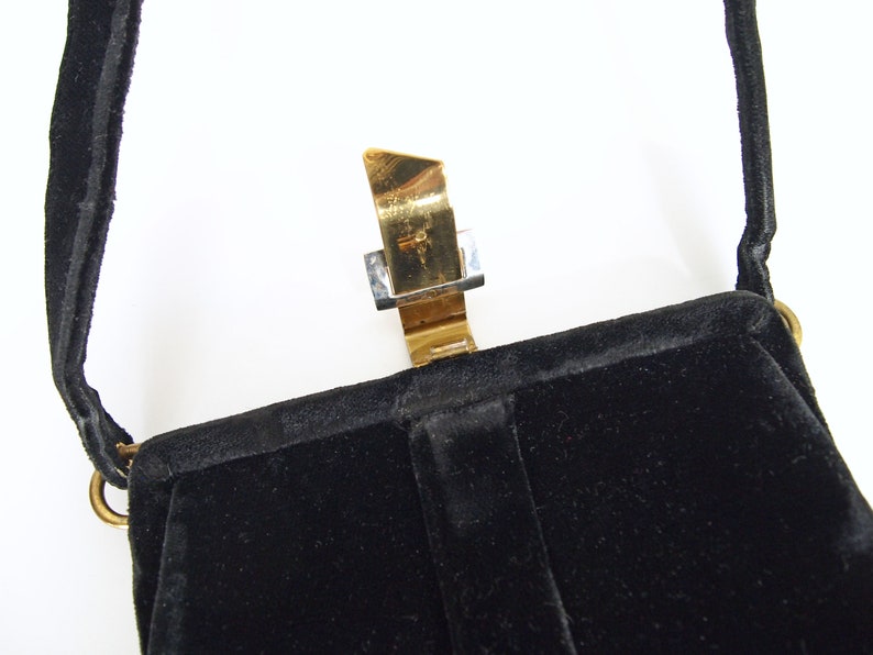 Puede incluir: Un bolso de noche de terciopelo negro con un cierre de metal dorado. El bolso tiene una sola correa.