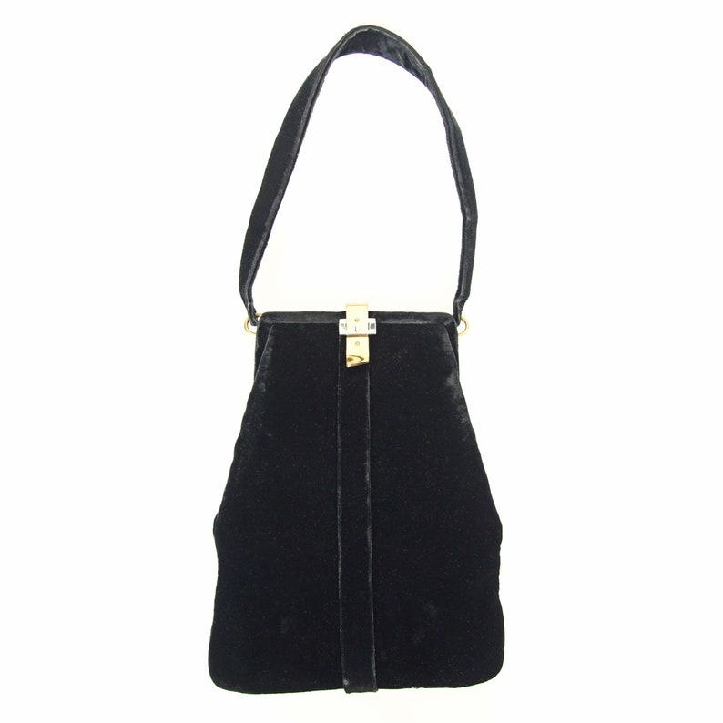 Puede incluir: Un bolso de mano de terciopelo negro con cierre dorado y una sola correa.