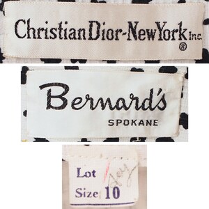 K&ouml;nnte beinhalten: Nahaufnahme von drei Kleidungsetiketten. Das obere Etikett lautet "Christian Dior-New York Inc." in schwarzem Text auf cremefarbenem Hintergrund. Das mittlere Etikett lautet "Bernard's Spokane" in schwarzer Schrift. Das untere Etikett lautet "Lot" und "Size 10".