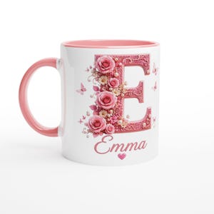 May include: White ceramic mug with a pink handle and interior. The letter "E" is decorated with pink roses, pearls, and butterflies. The name "Emma" is written below the letter, with a small heart.