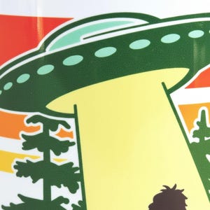 A green alien spacecraft hovers above a forest scene, with a yellow light emanating from the bottom of the image.