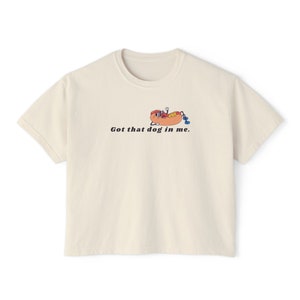 May include: Cream-colored t-shirt with a graphic of a hot dog relaxing with sunglasses and a blue drink. The text "Got that dog in me" is printed below the graphic in black.