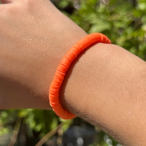 May include: A bright orange bracelet made of small, round beads. The bracelet is worn on a person's wrist.