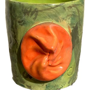 May include: A green ceramic mug with a large, orange, textured, swirl design on the front.