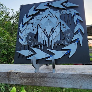Può includere: Un'opera d'arte murale stampata in 3D in nero e grigio che rappresenta un mostro con denti e artigli affilati. L'opera è montata su un supporto ed è esposta su uno sfondo di erba verde.