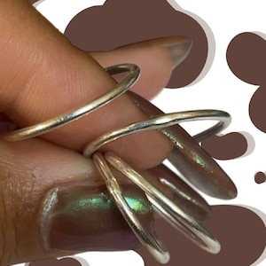 May include: A collection of silver rings in various sizes. The rings are thin and have a simple, minimalist design. The background is white with brown cow-print shapes.