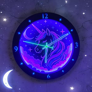 May include: A round, black wall clock with a glowing unicorn design. The clock face features a purple and blue unicorn with a crescent moon and stars. The clock hands are green, and the numbers are blue.