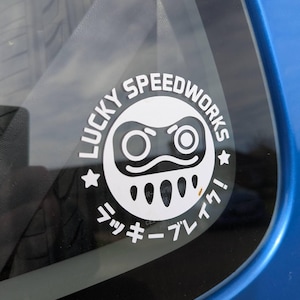May include: A white sticker with the text "Lucky Speedworks" in a circle with a black and white gamepad icon inside. The text "ラッキー アレイ!" is written in Japanese below the circle.