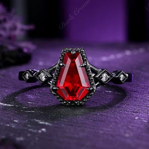 Könnte beinhalten: Ein schwarzer Ring mit einem großen, roten, sargförmigen Edelstein. Der Ring hat ein schwarzes Band mit kleinen, klaren Akzentsteinen. Die Worte "Dark Crown" sind im Hintergrund sichtbar.