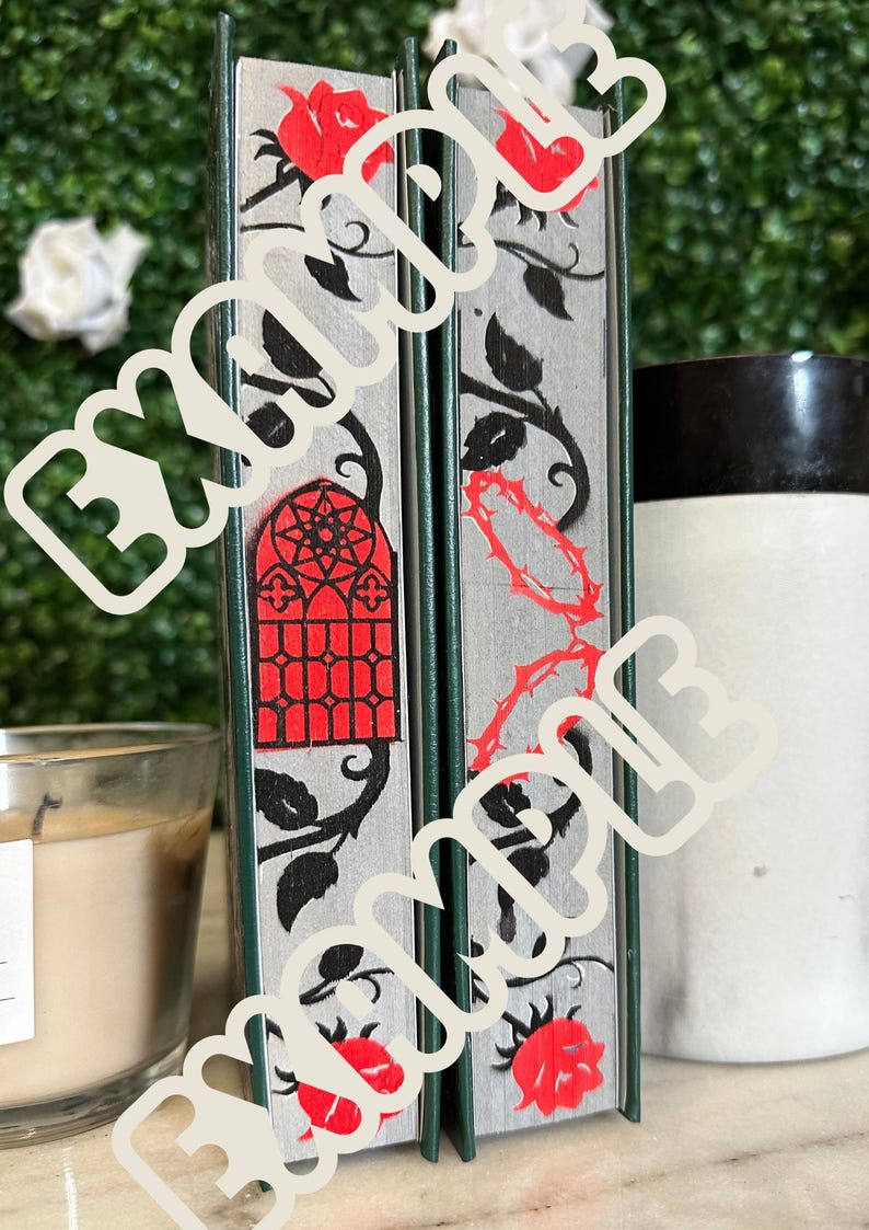 May include: Two decorative books with a silver background and black and red floral designs. The books have a green spine and red roses with thorns.