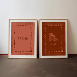 Puede incluir: Dos láminas rectangulares enmarcadas en madera clara. La lámina de la izquierda es de color terracota con el texto TI AMO. La de la derecha es marrón oscuro con un dibujo del Coliseo y el texto ROMA. Ambas tienen un borde festoneado.
