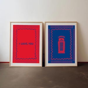 Puede incluir: Dos láminas de pared enmarcadas con marcos de madera clara. La lámina izquierda es roja con un borde azul ondulado y el texto "I LOVE YOU". La lámina derecha es azul con un borde rojo ondulado y una ilustración roja de una cabina telefónica.