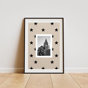 Puede incluir: Una lámina de arte enmarcada con fondo beige y un patrón repetitivo de estrellas negras. En el centro, una fotografía en blanco y negro muestra el edificio Chrysler y una señal de calle con el texto NEW YORK NEW YORK.