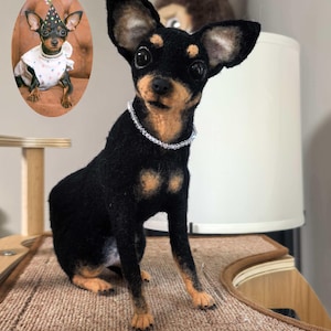 以下が含まれることがあります： 黒と茶色の手作りの犬の彫刻。ビーズの首輪があり、質感のある表面に置かれています。画像には、パーティーハットをかぶった犬の小さな額入りの画像が含まれています。犬の表情豊かな目に焦点を当てた、魅力的な芸術作品です。