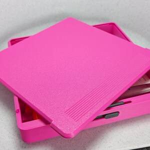 K&ouml;nnte beinhalten: Eine rosa Plastik-Aufbewahrungsbox mit Deckel. Der Deckel hat eine strukturierte Oberfl&auml;che und ist leicht ge&ouml;ffnet, so dass man das Innere der Box sehen kann.
