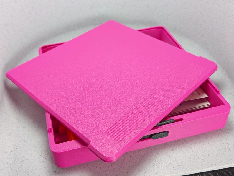 K&ouml;nnte beinhalten: Eine rosa Plastik-Aufbewahrungsbox mit Deckel. Der Deckel hat eine strukturierte Oberfl&auml;che und ist leicht ge&ouml;ffnet, so dass man das Innere der Box sehen kann.