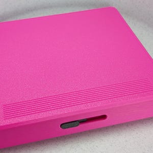 K&ouml;nnte beinhalten: Ein rechteckiges, hellrosa Etui mit strukturierter Oberfl&auml;che und einem kleinen schwarzen Verschluss.