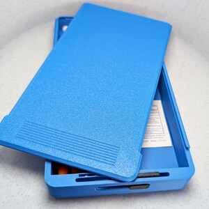 K&ouml;nnte beinhalten: Eine blaue Plastik-Aufbewahrungsbox mit einem strukturierten Deckel. Die Box ist ge&ouml;ffnet und enth&auml;lt ein wei&szlig;es Etikett.