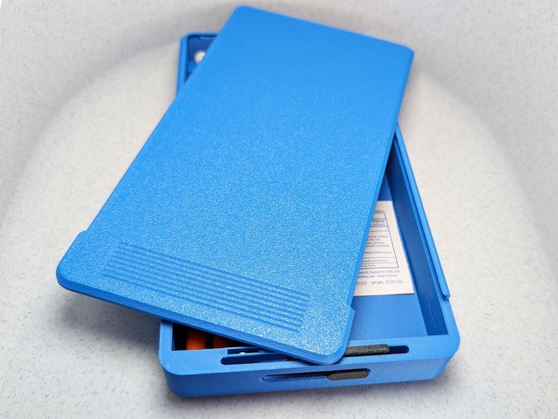 K&ouml;nnte beinhalten: Eine blaue Plastik-Aufbewahrungsbox mit einem strukturierten Deckel. Die Box ist ge&ouml;ffnet und enth&auml;lt ein wei&szlig;es Etikett.
