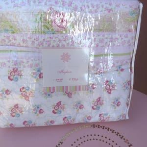 May include: A white and pink floral quilt with a label that reads "Magnolia Home Twin & Full".