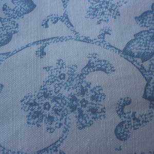 May include: A white fabric with a blue floral pattern. The pattern is made up of small, repeating flowers and leaves.