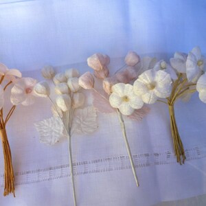 May include: Several bouquets of delicate, artificial flowers in shades of white and pink. The flowers have detailed petals and are bundled together with brown and silver stems, set against a white background.