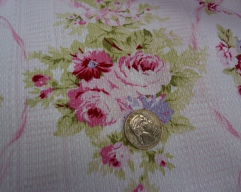 May include: A close-up of a pink and white floral fabric with a silver coin on top. The fabric has a textured surface and a repeating pattern of roses and leaves.
