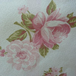 May include: A white fabric with a pink and green floral pattern. The fabric features a large pink rose with green leaves and smaller pink roses.