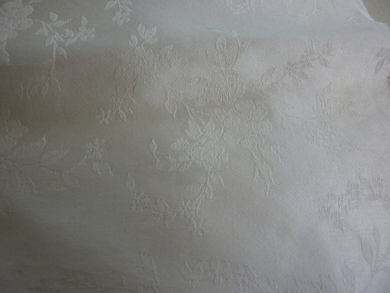 May include: White fabric with a subtle embossed floral pattern. The fabric has a smooth, silky texture.