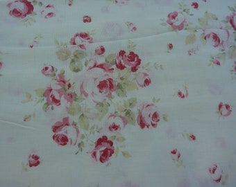 May include: White fabric with a pink and green floral pattern. The fabric features a repeating design of roses and leaves.