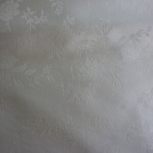 May include: White fabric with a subtle embossed floral pattern. The fabric has a smooth, silky texture.