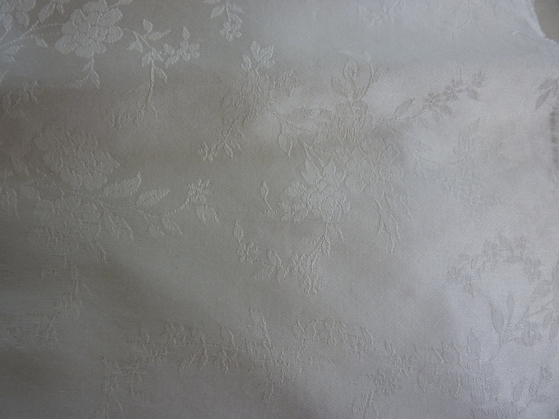 May include: White fabric with a subtle embossed floral pattern. The fabric has a smooth, silky texture.