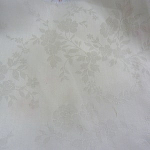 May include: White fabric with a subtle embossed floral pattern. The fabric has a smooth, slightly textured surface.