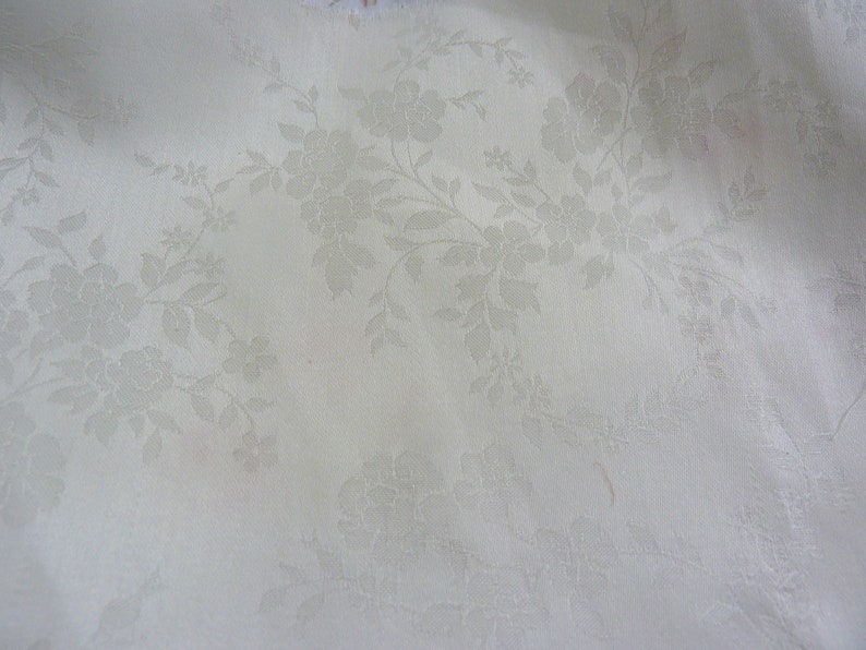 May include: White fabric with a subtle embossed floral pattern. The fabric has a smooth, slightly textured surface.