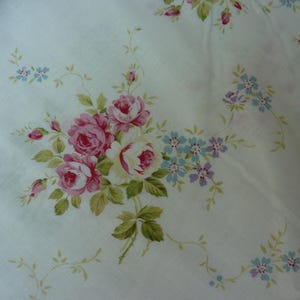May include: White fabric with a repeating pattern of pink roses and blue flowers. The roses are clustered together and have a vintage look.