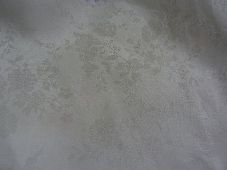 May include: White fabric with a subtle embossed floral pattern. The pattern features delicate flowers and leaves.