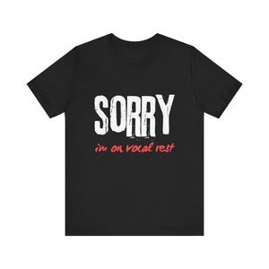 May include: Black t-shirt with white text that reads "SORRY i'm on vocal rest" in a distressed font. The text "i'm" is in red.