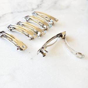 May include: A set of ten silver metal hair clips. The clips are all the same size and shape, and they have a simple, elegant design.