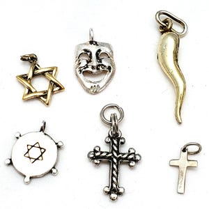 May include: A collection of six metal charms including a gold-tone Star of David, a silver-tone theatrical comedy mask, a gold-tone curved horn, a silver-tone circular charm with a star, a silver-tone ornate cross, and a small silver-tone plain cross.