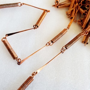 May include: A copper-colored chain necklace made of linked spring coils. The necklace is made of multiple small, linked coils of copper wire.