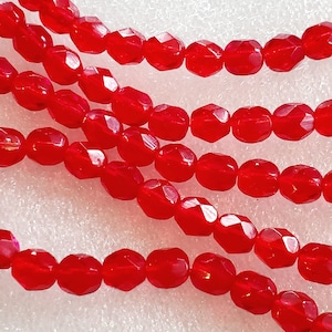 Könnte beinhalten: Eine Strähne roter facettierter Glasperlen. Die Perlen sind oval geformt und haben eine glänzende Oberfläche.