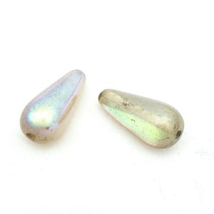 May include: Two iridescent teardrop-shaped beads. The beads have a pearlescent finish with hints of purple, green, and gold. They are smooth and rounded, with a small hole at the top for stringing.