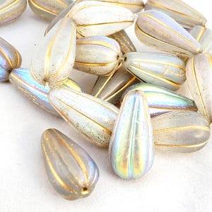 Könnte beinhalten: Eine Sammlung von tropfenförmigen, irisierenden Perlen. Die Perlen haben eine perlmuttartige Oberfläche mit goldfarbenen Streifen. Diese dekorativen Perlen sind ideal für die Schmuckherstellung und Bastelprojekte.